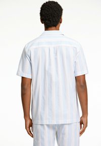 Camisa de manga corta con rayas verticales en azul y blanco. Fabricada con tejido ligero, presenta un dobladillo recto y una textura suave.