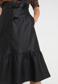 Sort læderskirt med en flared kant, bælte detalje ved taljen og sidelommer. Glat tekstur med en subtil glans.