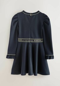 Robe bleu marine avec une jupe évasée, des manches longues bouffantes et des poignets volantés. Présente une bande de logo dorée le long de la taille et une fermeture éclair au dos.