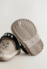 Beżowe klapki z czarnym paskiem, logo na zewnętrznej stronie i otworami wentylacyjnymi. Podeszwa z bieżnikiem w zygzakowaty wzór. Trwały materiał, lekka konstrukcja.