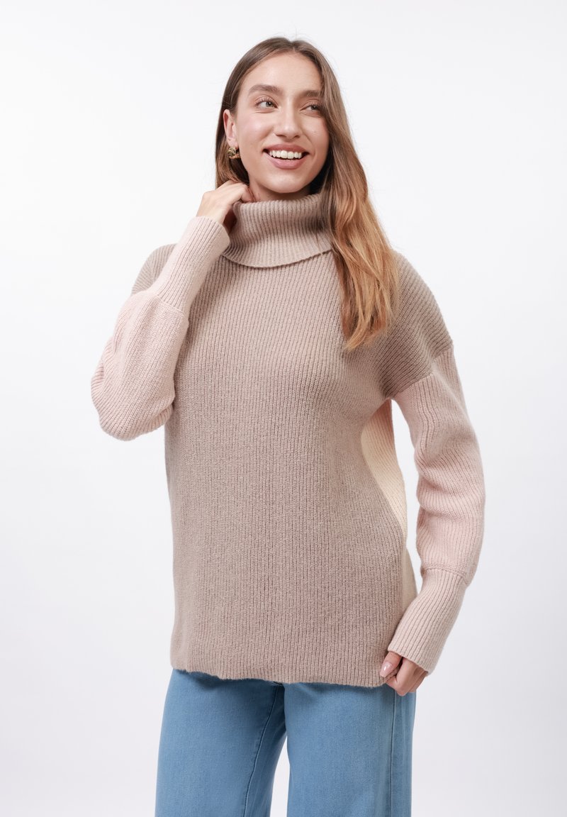 Beżowy sweter z golfem o plecionym wzorze, z opadającymi ramionami i długimi rękawami. Posiada przejście kolorystyczne do jaśniejszego odcienia różu.