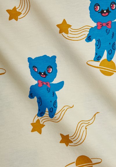 Μπλε καρτούν αρκούδα με ροζ παπιγιόν ανάμεσα σε πορτοκαλά π εφταστέρια και πλανήτες με δαχτυλίδι σε μπεζ φόντο υφάσματος.