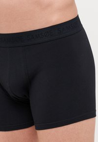 Sorte bomullshorts med en glatt tekstur, med et logo-embossert elastisk liv. Sittende design med dekning til midten av låret.