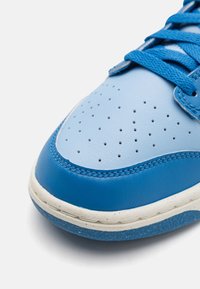 Blå lædersneakers med en lyseblå tåkappe, perforeret design og blå snørebånd; har en hvid mellemsål og tekstureret ydersål.