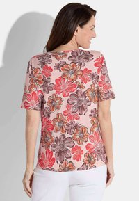 Bloemige top met korte mouwen, met een roze achtergrond en koraal, rode en bruine bloemen. Zachte stof met een losse pasvorm en ronde halslijn.