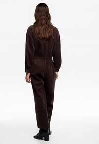 Mono marrón con mangas largas, cintura elástica y tejido texturizado. Combinado con botas de tacón negras para mayor altura.