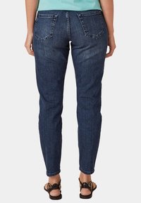 Tummansiniset farkut, joissa on slim fit -leikkaus, takataskut ja hieman kapenevat lahkeet, yhdistettynä ruskeisiin sandaaleihin.