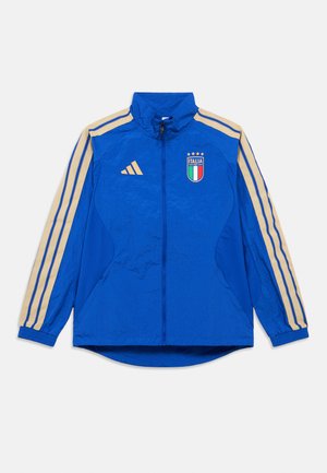 Blå sportsjakke med lynlås og beige striber på ærmerne, Italiens fodboldemblem og Adidas-logo på brystet.