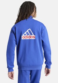 Blauwe crewneck sweatshirt met een rood-wit adidas-logo op de achterkant, ribgebreide boorden en een casual pasvorm. Gemaakt van zacht textielmateriaal.