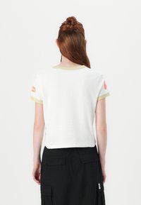 White cropped t-shirt with yellow trim and orange logo detail on the left sleeve. Smooth cotton fabric, relaxed fit.