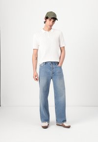 Hvid kortærmet ribbet polo-shirt, lys blå vidde denimbukser, olivengrøn kasket og lyse sko med brune såler.