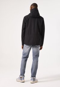 Black hooded jacket with a sleek design, made from smooth fabric, worn over light blue jeans, paired with gray and blue sneakers.