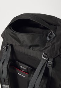 Sac à dos noir avec une ouverture par le haut, en tissu texturé, avec des bretelles ajustables et des sangles visibles. Présente des compartiments intérieurs étiquetés OPTIFIT et NEXTVENT.