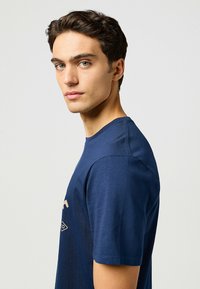 Navyblå t-shirt i bomull med rund halsringning och korta ärmar. Designen inkluderar en liten logo tryckt på framsidan.