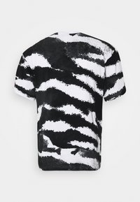 Svart och vit abstrakt zebramönstrad t-shirt med kort ärm, sedd bakifrån på en enfärgad bakgrund.