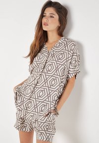 Musteroberteil mit kurzen Ärmeln und Shorts in hellbeige mit dunklen geometrischen Designs. Der Stoff wirkt glatt und hat eine lockere Passform.