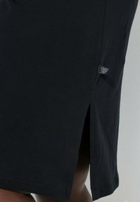 Gonna di cotone nera con dettaglio di spacco laterale. Presenta un'etichetta con accenti metallici, una texture liscia e un design semplice.