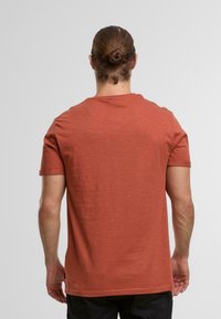 Rdzawoczerwony t-shirt z krótkim rękawem, wykonany z miękkiego, teksturowanego materiału. Posiada okrągły dekolt i luźny krój, z minimalnymi detalami.