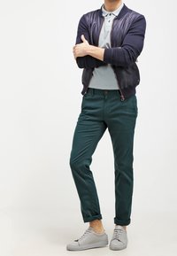 Avslappnad outfit med en marinblå bomberjacka, ljusgrå polo, mörkgröna chinos och ljusgrå sneakers med runda snören.