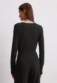 Zwarte langemouwtop met een ronde halslijn, aansluitend in de taille, gemaakt van een glad materiaal. Draag het met hooggerokte zwarte broeken.