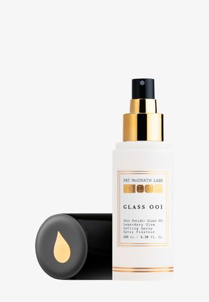 Transparent glass spray bottle with gold accents, black nozzle, and label featuring product name and details. Cap has a gold drop design.