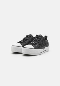 Schwarze Sneakers mit strukturiertem Obermaterial, weißer Gummispitze und strukturiertem Plateausohle. Mit Schnürsenkeln und einer Zuglasche an der Ferse.