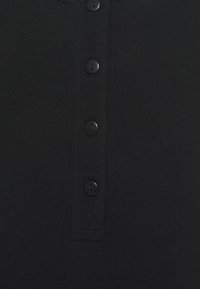 Schwarzes Stoffoberteil mit einer Knopfleiste, die fünf schwarze Knöpfe umfasst. Das Material ist glatt und leicht dehnbar mit sichtbaren Nähten.