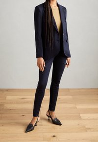 Námořnický blejzr a odpovídající úzké kalhoty v kombinaci s černými lodičkami na podpatku. Blejzr má jednoramenný design a kapsy.