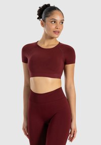 Mørkerød træningssæt bestående af en kortærmet crop top og højtaljede leggings, lavet af et glat, strækbart stof med dekorerende syninger.