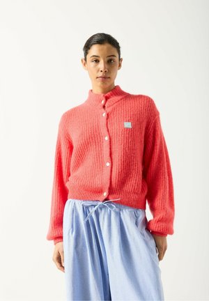 Cardigan lavorato a maglia color corallo con tessuto strutturato, collo alto e chiusura con cinque bottoni, abbinato a pantaloni azzurri con coulisse.