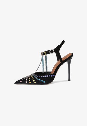 Black suede high-heeled shoe with pointed toe, adorned with colorful gemstones and chains, featuring a slingback strap and a stiletto heel.