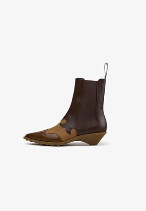 Stivale in pelle marrone fino alla caviglia con pannello anteriore decorativo color cuoio, punta appuntita, pannelli laterali elastici, linguetta per tirare e tacco basso inclinato.