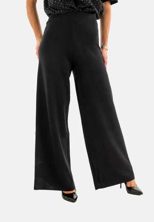 Pantaloni neri a gamba larga realizzati in materiale morbido, con un'alta vita e una texture liscia. Abbinati a tacchi a punta neri.