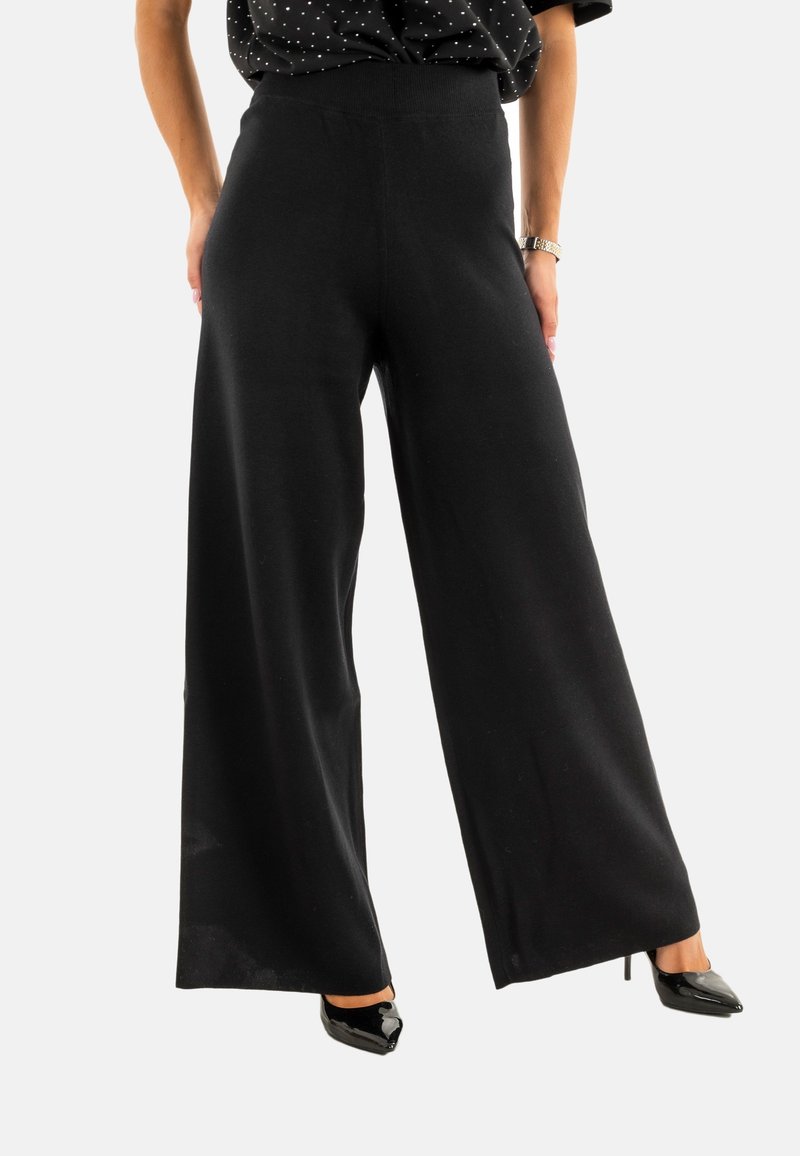 Pantalones de pierna ancha negros, hechos de un material suave, con una cintura alta y una textura lisa. Combinados con tacones de aguja negros.