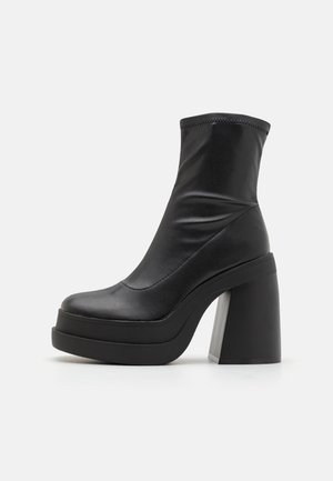 Sort ankelstøvle lavet af syntetisk materiale, med et elegant design, chunky hæl og plateau-sål. Glat tekstur med minimale syningsdetaljer.