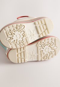 Weiße Gummisohlen mit strukturierten Griffmustern und verspielten Spritzdesigns. Akzente in Rot und Hellblau entlang der Ränder.