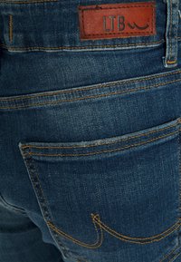 Jeans de ganga azul com um tecido texturizado, costura proeminente e uma etiqueta de marca de couro rotulada "LTB" na cintura.