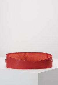 Cintura in pelle rossa con esterno liscio e interno morbido simile al feltro. Presenta un design attorcigliato e una chiusura regolabile.