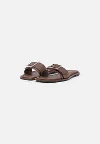Sandalias planas marrones con doble correa, que incluyen una hebilla rectangular plateada. Material de textura suave, diseño de perfil bajo y suelas lisas.