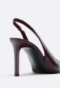 Burgundy slingback heel with a glossy finish, pointed toe, and a high stiletto heel; textured leather material and elastic strap detail.