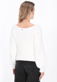White knitted sweater with a soft, fluffy texture, featuring wide sleeves and a boat neckline, paired with black high-waisted jeans.
