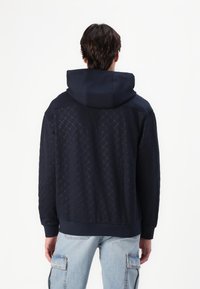 Felpa navy con un motivo testurizzato, dotata di cappuccio con cordino e polsini a costine. La vista posteriore mostra un design in tessuto contrastante.