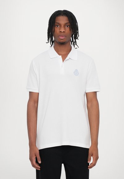 Witte polo met korte mouwen met een klein blauw geborduurd logo op de linkerkant van de borst, met een kraag en rechte zoom.