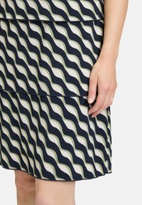 Granatowa sukienka z zielonym i białym falistym wzorem. Wykonana z gładkiego materiału z warstwowym designem, charakteryzująca się stylowym hemem i dopasowanym krojem.