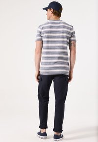 Camisa de manga corta a rayas en gris y azul marino, combinada con pantalones cargo oscuros. Incluye una gorra azul y zapatillas casuales azul marino.