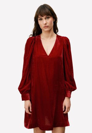 Rode fluwelen jurk met een diepe V-hals, lange geplooide mouwen en een losse pasvorm. Gladde textuur en zachte glans versterken het geheel.