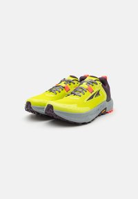 Zapatillas de running amarillas brillantes con un upper texturizado, acentos morados, detalles reflectantes y una suela gris rugosa para tracción.