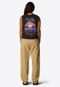 Zwarte mouwloze top met kleurrijke grafische print op de achterkant met de tekst "Never Stop Exploring", gecombineerd met beige wijde broek.
