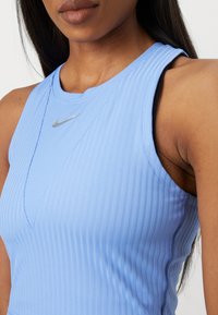 Hellblaue rippte Sporttanktop mit hohem Kragen und silbernem Nike-Logo. Verfügt über ein schlankes Design und strukturierten Stoff.