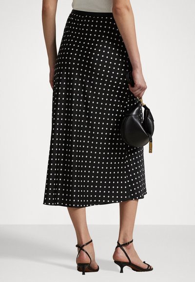 Black knee-length skirt with white polka dots, featuring a solid waistband. Pairing with a small black handbag and strappy black heels.